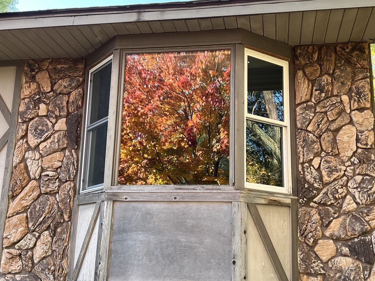 Bay window on a stone-faced home with a film on the glass, glaring bright orange in the sunlight