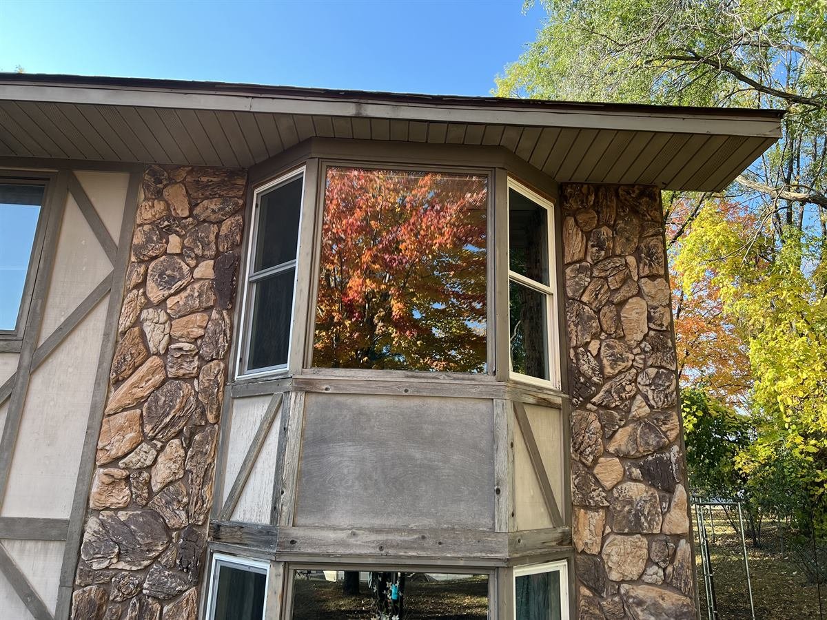 Front of a home with a film on the window glass, catching the sunlight as a bright haze
