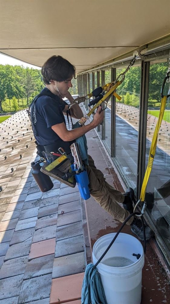Caleb Walker, owner of Walker Window Works, cleaning upper-story windows with an extension pole from a roof